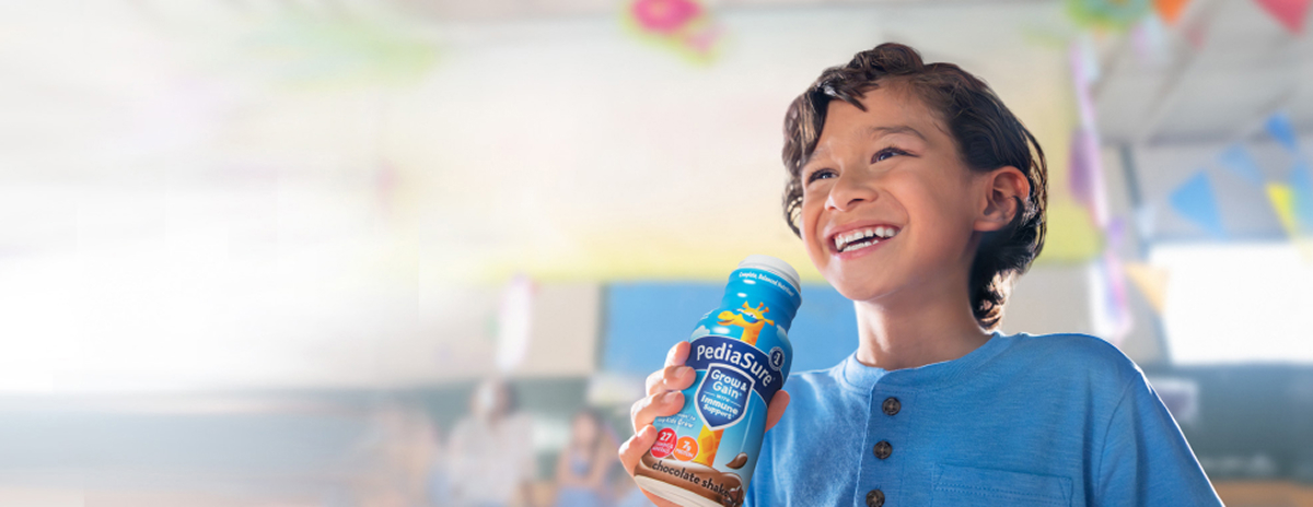 Boy drinking Chocolate PediaSure® shake with vitamins and other nutrients to help him grow.